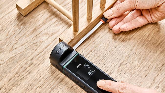 Küchenregal aus Tellerhaltern bauen mit präziser Holzarbeit, Person misst den Abstand zwischen Holzleisten mit einem digitalen Messgerät zur exakten Montage der Tellerhalter