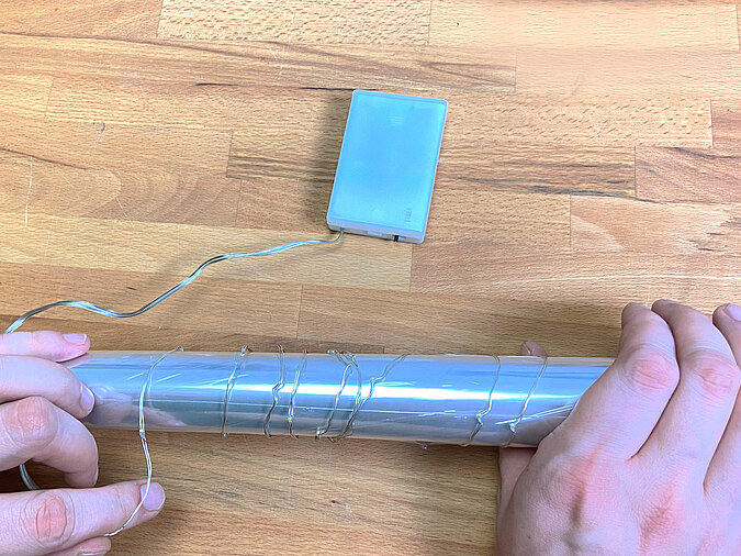 Lichterkette wird um eine Papprolle gewickelt, das erleichtert später die Einführung in die Getränkedose. Das Batteriefach liegt daneben auf der Werkbank.“