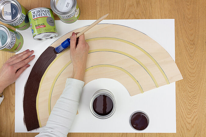 Wandleuchte im Regenbogen-Design bauen – Holz-Regenbogen wird mit brauner Farbe gestrichen, DIY-Schritt zur Gestaltung der bunten Bögen.