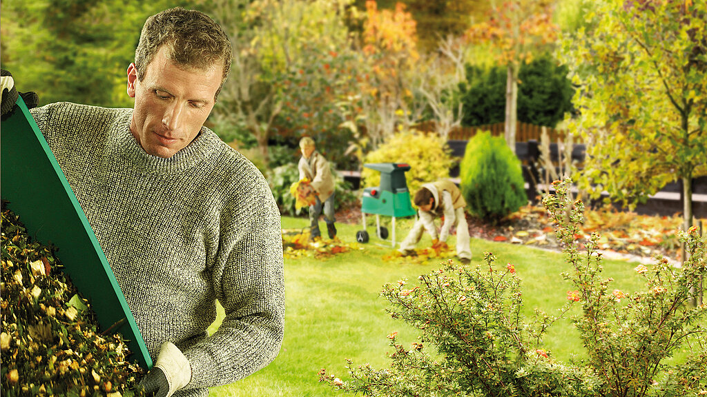 Gartenarbeiten Frühling: Rasenkante im Garten mit Rasentrimmer schneiden während im Hintergrund Gartenarbeit erledigt wird