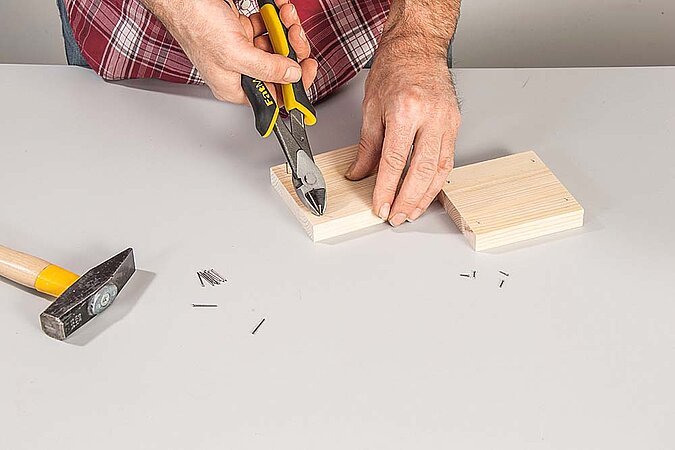Kleine Nägel werden mit einer Zange in ein Holzteil für ein Regal am Raumteiler aus Birkenstämmen gedrückt
