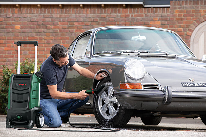 Auto selbst waschen Oldtimer – Mann beseitigt groben Schmutz mit Waschbürste um Lack und Felgen schonend zu reinigen und den Glanz des Fahrzeugs zu bewahren.