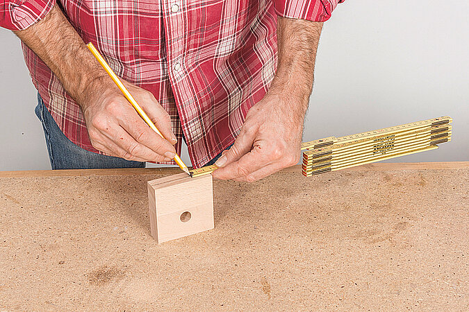Wandgarderobe aus Kickerfiguren bauen mit Maßband und Bleistift beim Anzeichnen der Bohrpositionen auf dem Holz-Abstandshalter