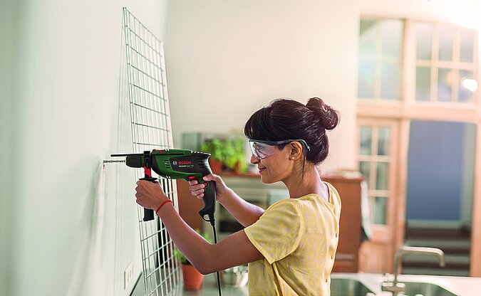 Frau bohrt mit Schlagbohrmaschine ein Loch in die Wand