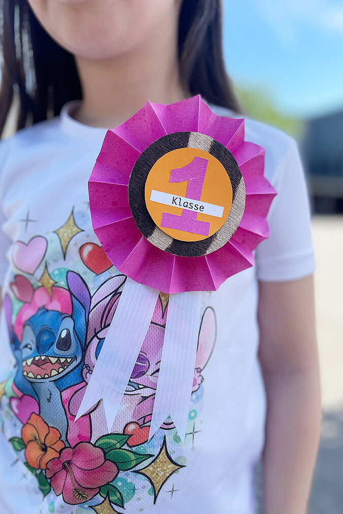 Einschulung Orden basteln mit pinker DIY Schultüten Ordenrosette für die 1. Klasse am T Shirt getragen