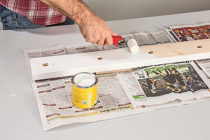 Holzbrett für einen Raumteiler aus Birkenstämmen wird auf Zeitungspapier mit weißer Farbe gestrichen
